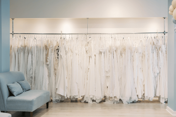 Bright bridal boutique with rows of white wedding gowns on racks, a pale blue sofa, and soft lighting creating an elegant, serene mood.