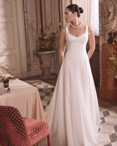 A woman in a white gown stands elegantly in a room with classic decor. 