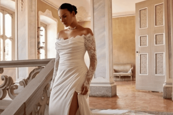 A woman wearing an elegant white wedding dress with lace sleeves, standing on a staircase, showcasing timeless style amidst wedding color trends 2025