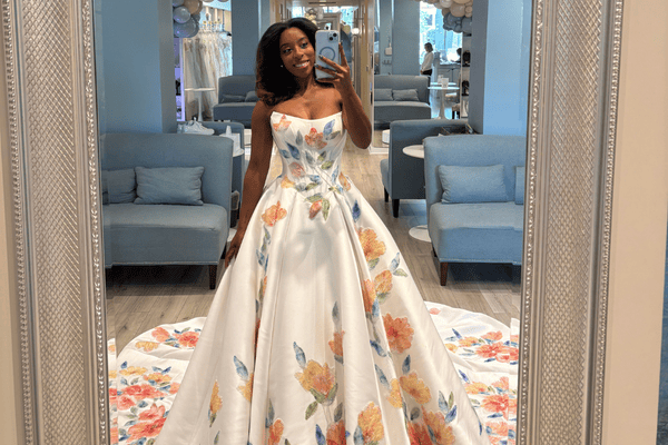 Bride taking a mirror selfie in a bridal boutique wearing a strapless ball gown wedding dress with colorful floral print and a full train.