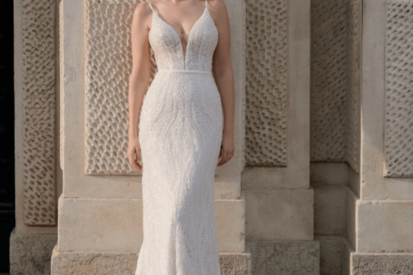 A bride wearing a sheath wedding dress, leaning against a concrete wall with geometric cutouts