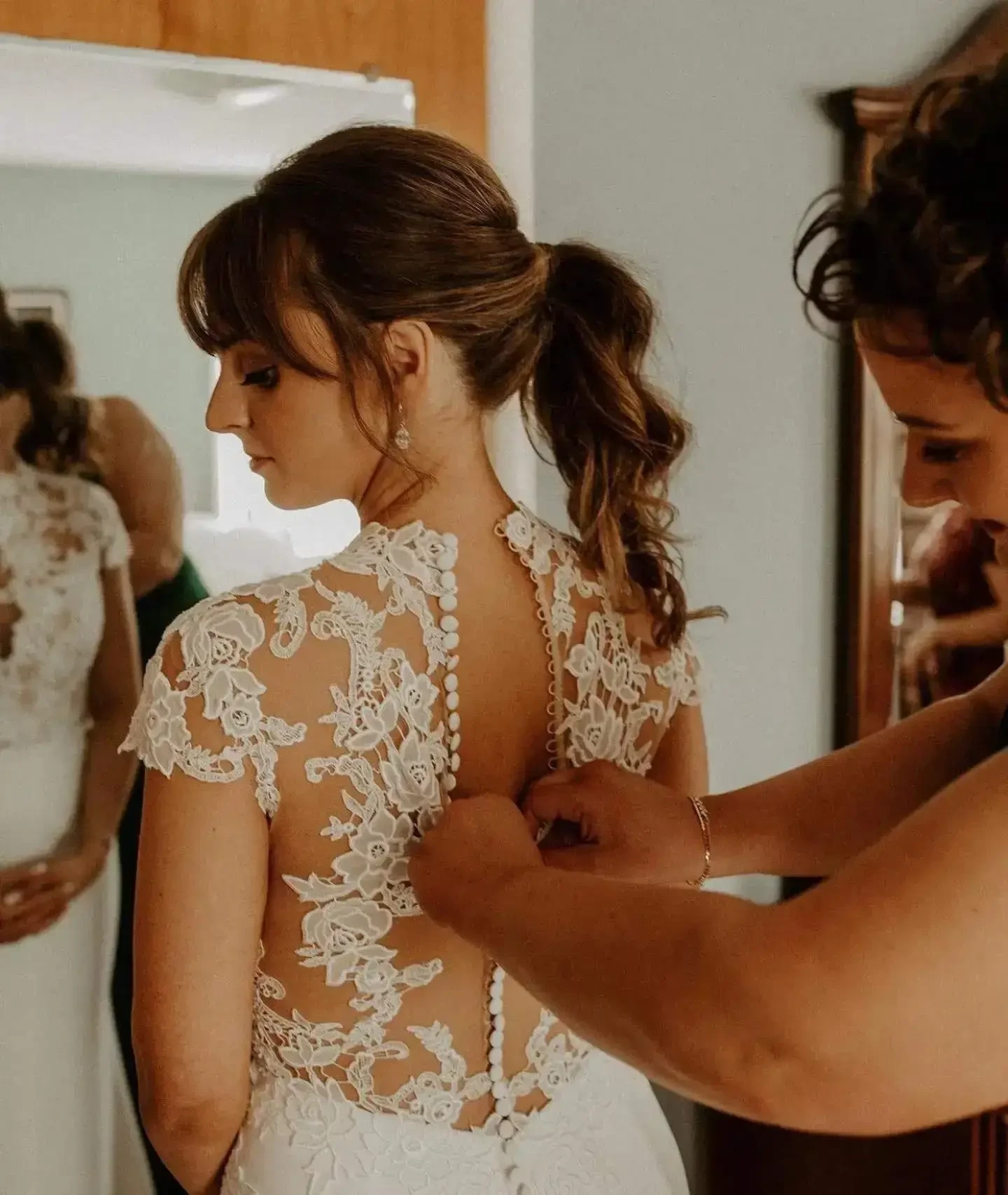 Bride having the buttons fastened on a lace illusion back wedding dress during bridal preparations at Belle Amour Bridal