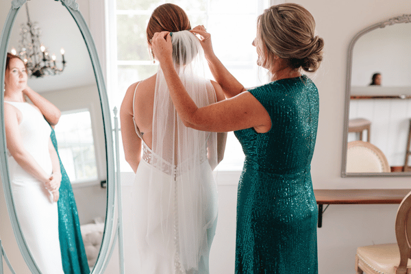 Mother of the bride adjusting the bride&rsquo;s veil in front of a mirror