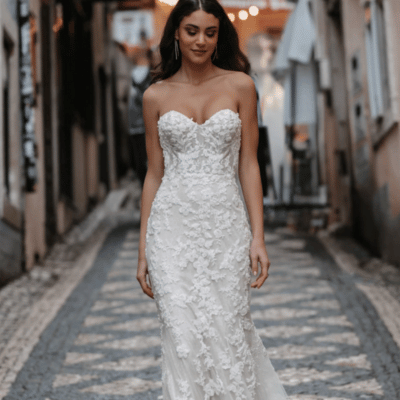 A woman wearing a strapless sheath wedding dress with floral details, walking down a cobblestone street, perfectly embodying a look from a wedding dress style guide. This unique wedding gown highlights the elegance of bridal personality styles, offering inspiration for those seeking a timeless yet distinctive design.