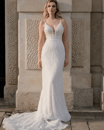 A woman in a stunning white wedding dress with a fitted silhouette and beaded details, standing outdoors. 