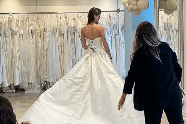 A bride trying on her wedding dress while her stylist observes the fitting