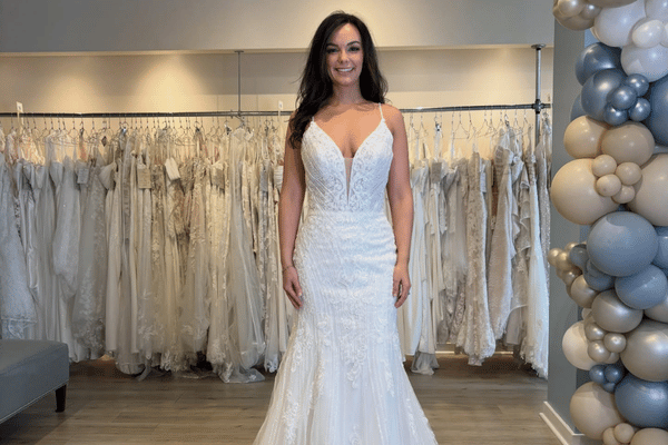 Bride wearing a fitted lace wedding dress with thin straps and deep V neckline in a bridal boutique
