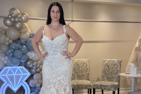 Bride trying on fitted lace sample sale wedding dress with wide straps in bridal shop