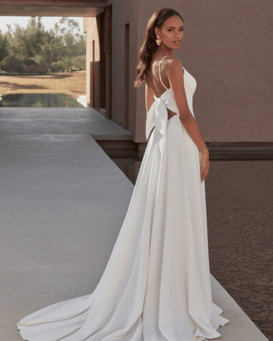 A bride in a white wedding dress with a bow on the back, standing outdoors. 