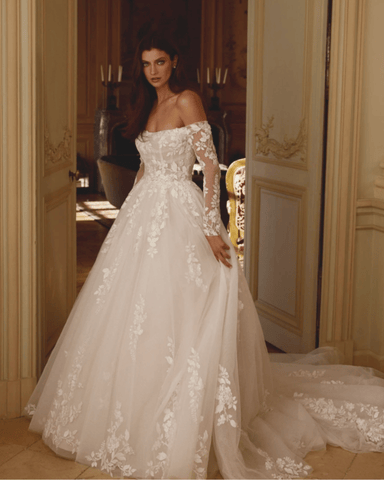 A woman holding her ball gown wedding dress standing by the door looking straight at the camera