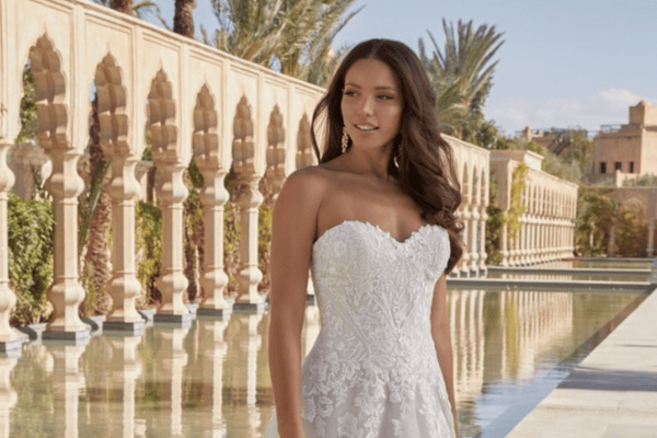 A bride showcases one of the best necklines for a bridal look in a strapless wedding dress, standing by a reflective pool with palm trees in the background.
