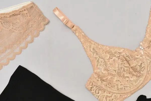 Beige lace bra and matching lace underwear displayed on a light surface alongside black underwear.