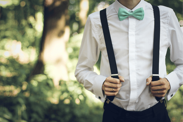 A groom with a button-down white shirt and suspenders 