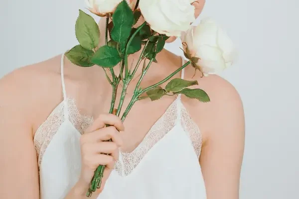 Woman in a dark blue floral dress looking at a white wedding gown among several bridal dresses hanging on a rack.