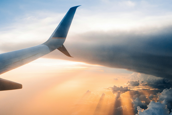 Airplane wing above the clouds at sunrise, representing air travel for a destination wedding and safely transporting a wedding dress.