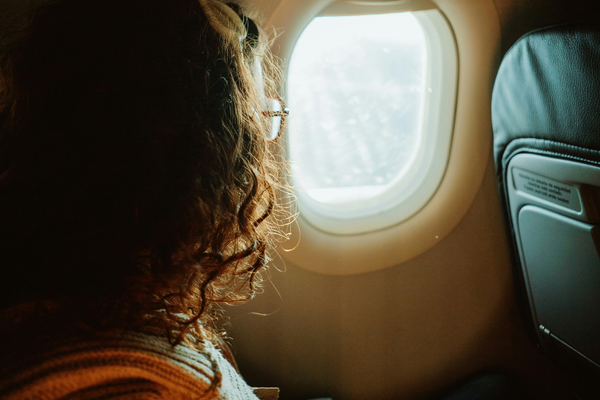 Bride-to-be sitting by an airplane window during a flight, symbolizing wedding travel and destination wedding preparations.