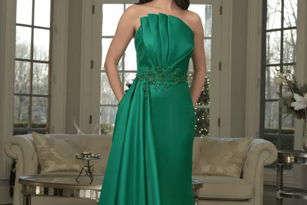 Woman wearing a strapless emerald green mother of the bride gown with pleated bodice, floral beaded waist, and draped skirt.
