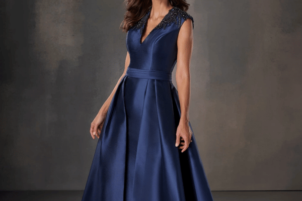 Woman wearing a navy blue A-line mother of the bride gown with cap sleeves, lace neckline, and satin skirt.