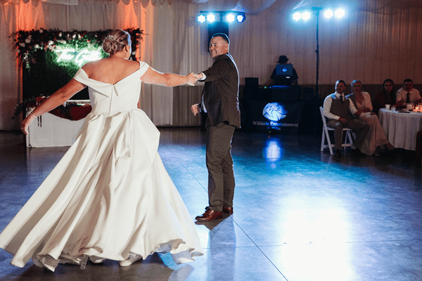 A bride in a white wedding dress showcasing mobility dances with a groom in a suit, smiling at each other in a decorated venue.