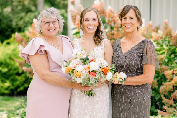 Bride holding a bouquet and posing with her mother and another family member on her wedding day.